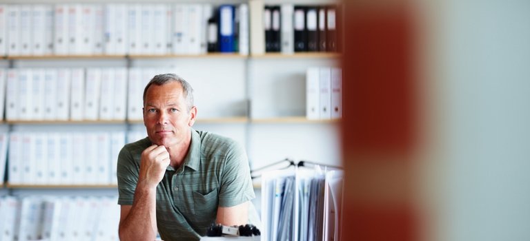 Mann sitzt vor Regalen voller Akten am Schreibtisch im Büro