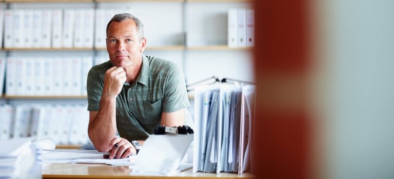 Mann sitzt vor Regalen voller Akten am Schreibtisch im Büro