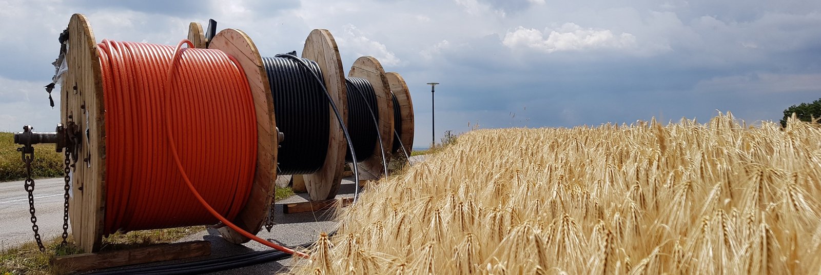 Trommeln mit Glasfaserkabeln am Rand eines Weizenfeldes