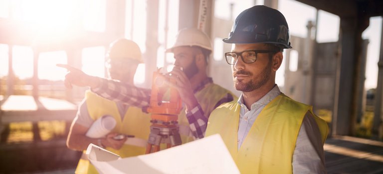 Bauarbeiter mit Plänen und Vermessungsgeräten auf Baustelle