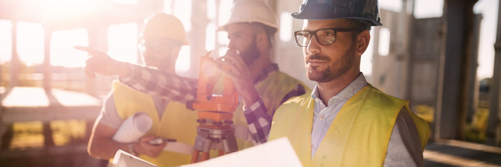 Bauarbeiter mit Plänen und Vermessungsgeräten auf Baustelle