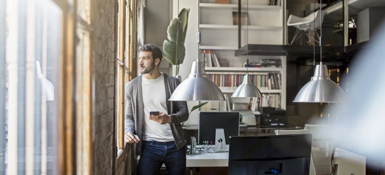 Junger Unternehmer steht in Start-up-Büro am Fenster