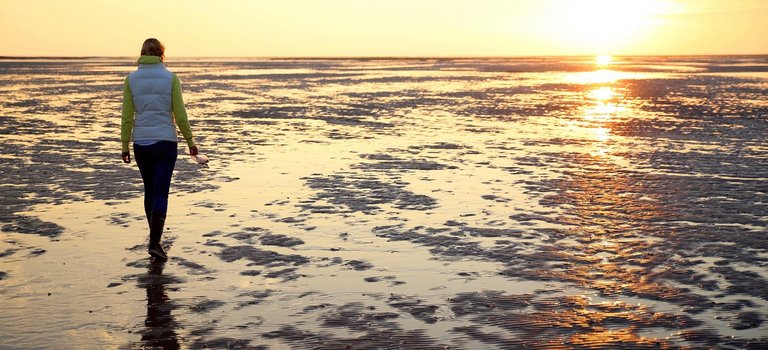 Frau geht im Sonnenuntergang im Watt spazieren