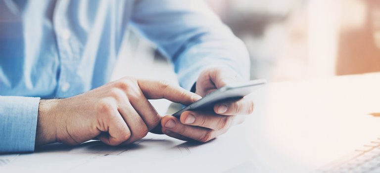Mann am Schreibtisch tippt auf Handy