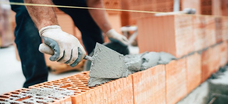 Maurer baut mit Kelle und Zement eine Mauer