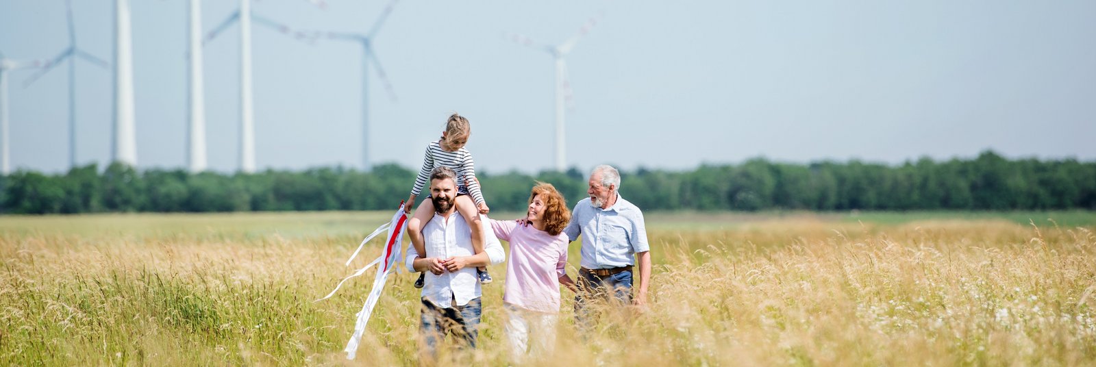 Drei Generationen einer Familie spazieren vor Windkraftanlagen durch ein Kornfeld