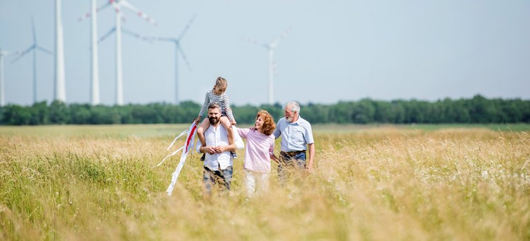 Drei Generationen einer Familie spazieren vor Windkraftanlagen durch ein Kornfeld