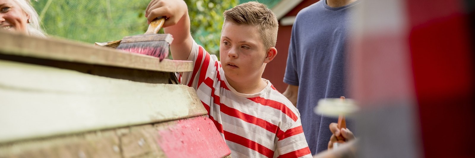 Kind mit Behinderung und junger Mann streichen Holzbauprojekt